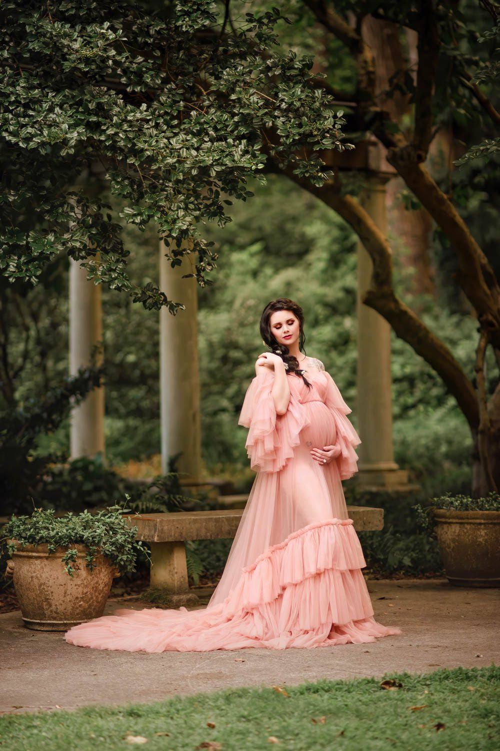 Pregnant woman in a blush tulle gown with the Cator Woolford Gardens colonnade in the background in Atlanta, GA.