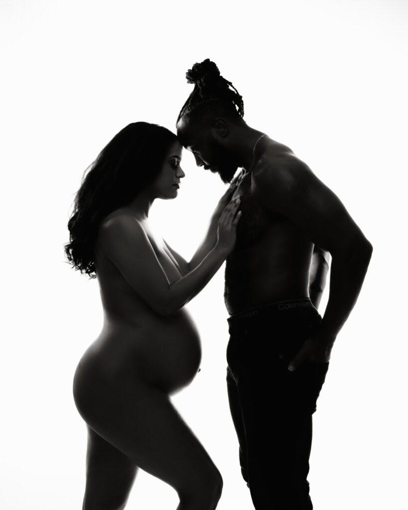 Black couple standing nude forehead to forehead in black-and-white portrait against bright white studio backdrop.