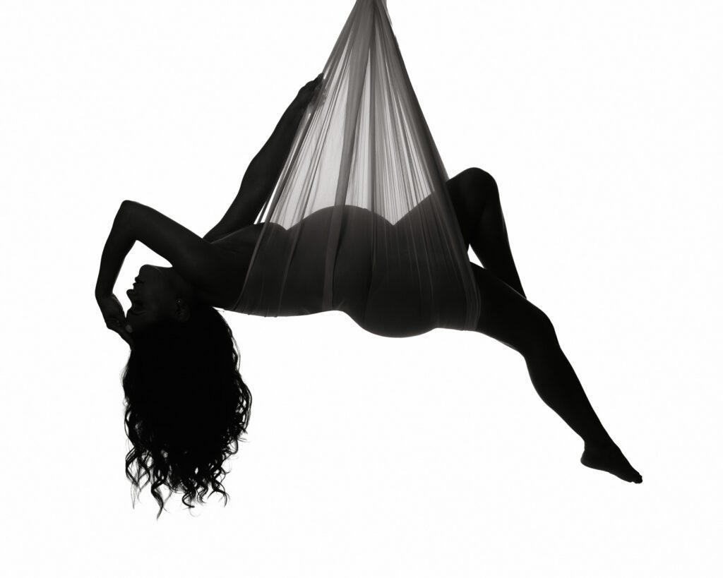 Pregnant woman suspended in sheer fabric against a bright white background during a Marietta maternity photography session.