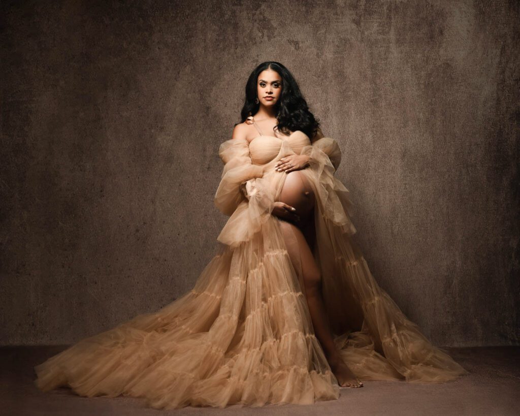 Expecting mother in a beige tulle gown cradling her bare belly during a Marietta maternity photography session.