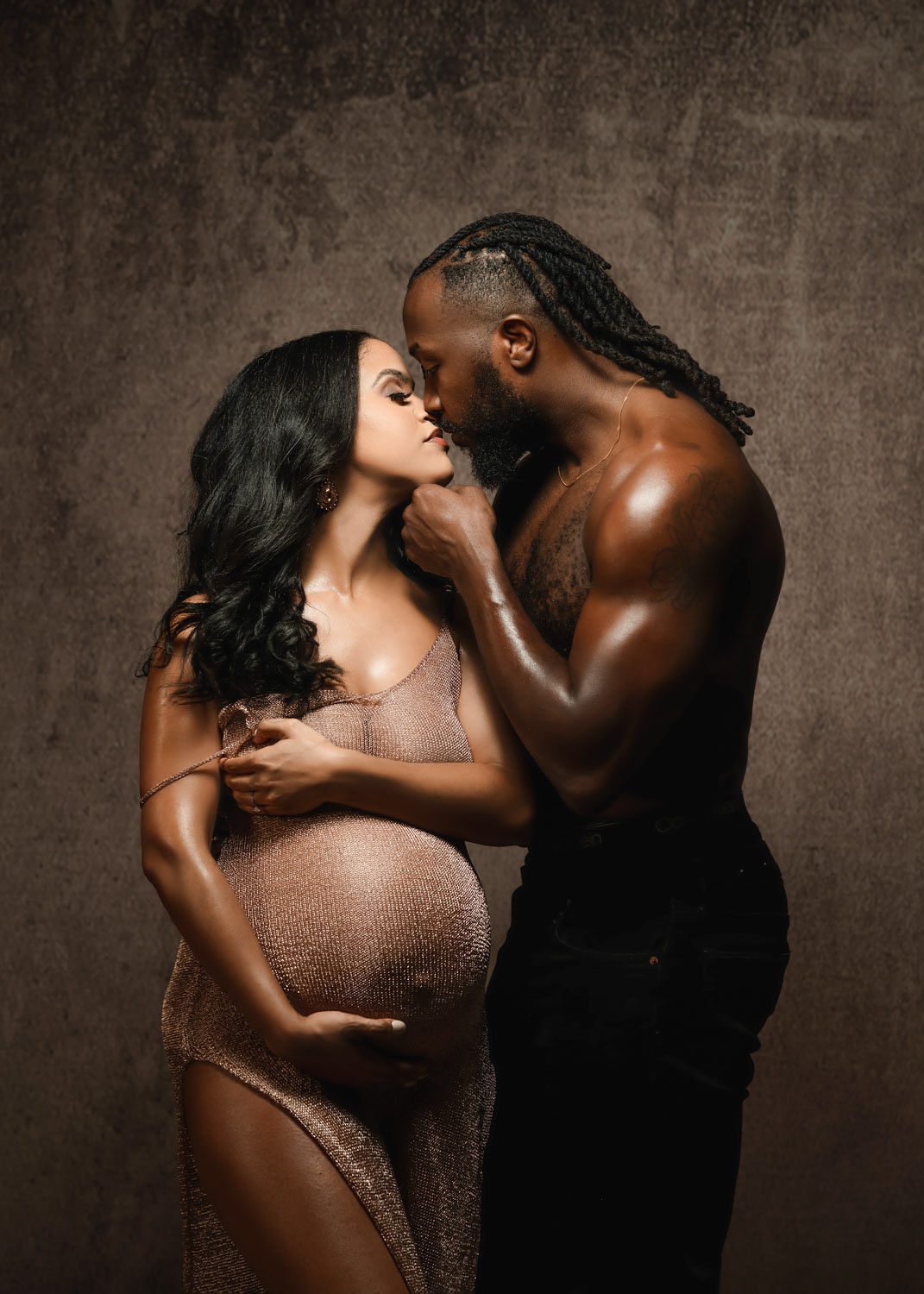 Pregnant woman in sheer brown gown kisses shirtless partner during a Marietta maternity photographer session.