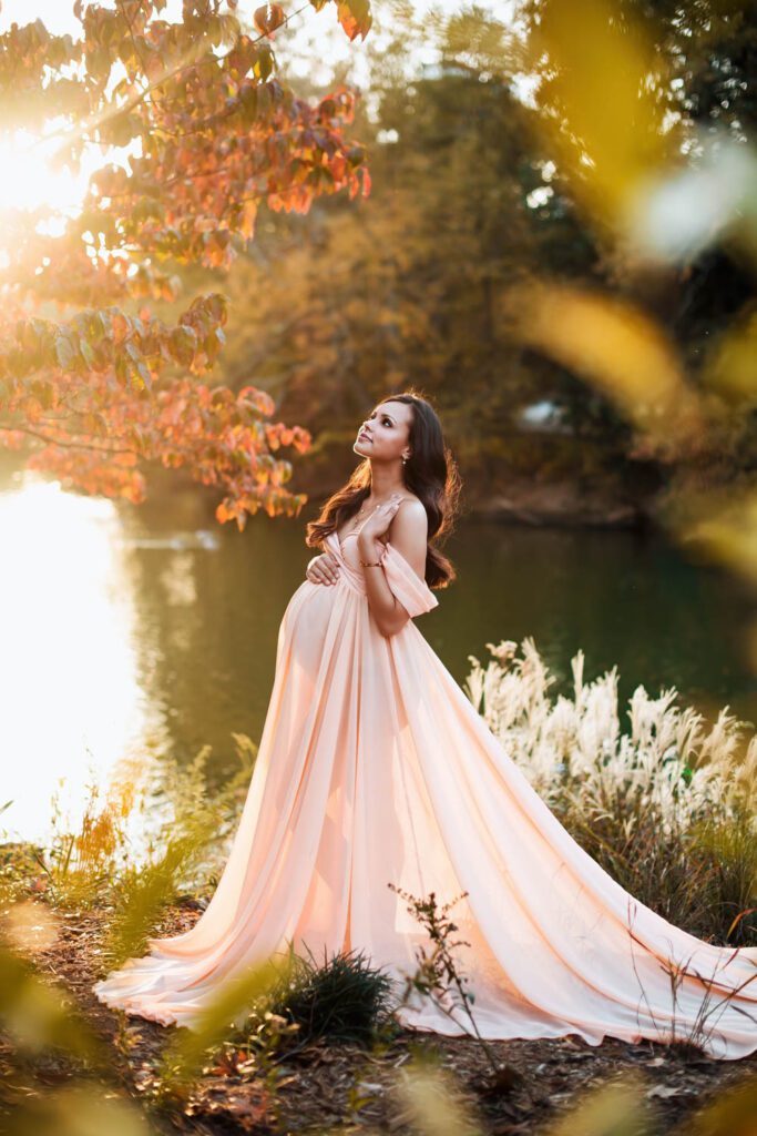 Pregnant woman in peach gown poses beside Lake Clara Meer at Piedmont Park in Atlanta, GA.