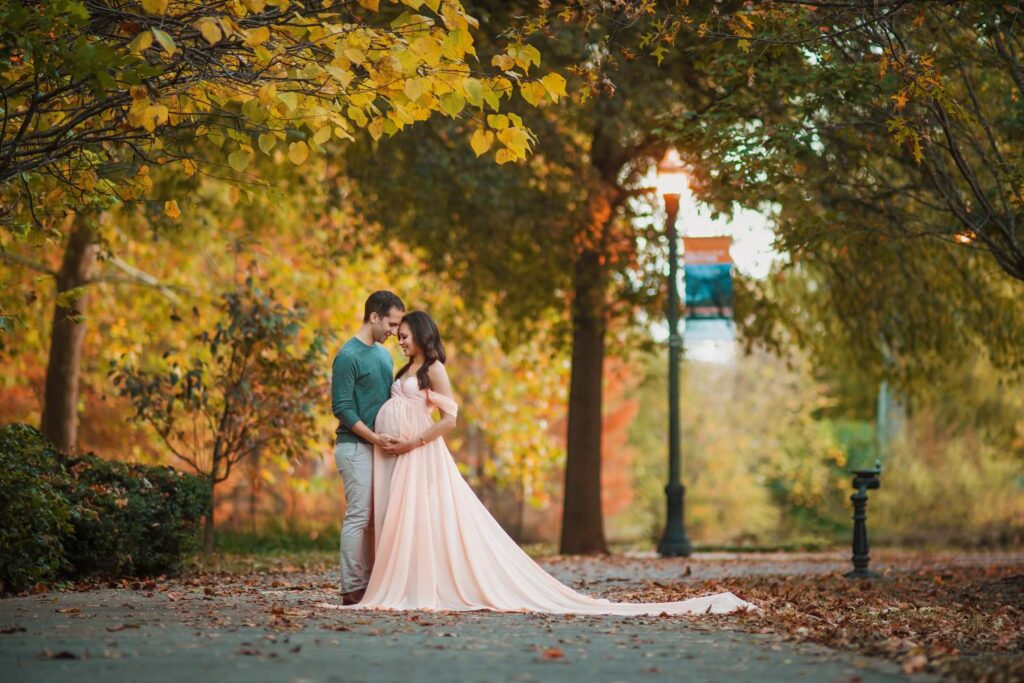 Expecting couple embraces on an autumn path surrounded by colorful fall trees