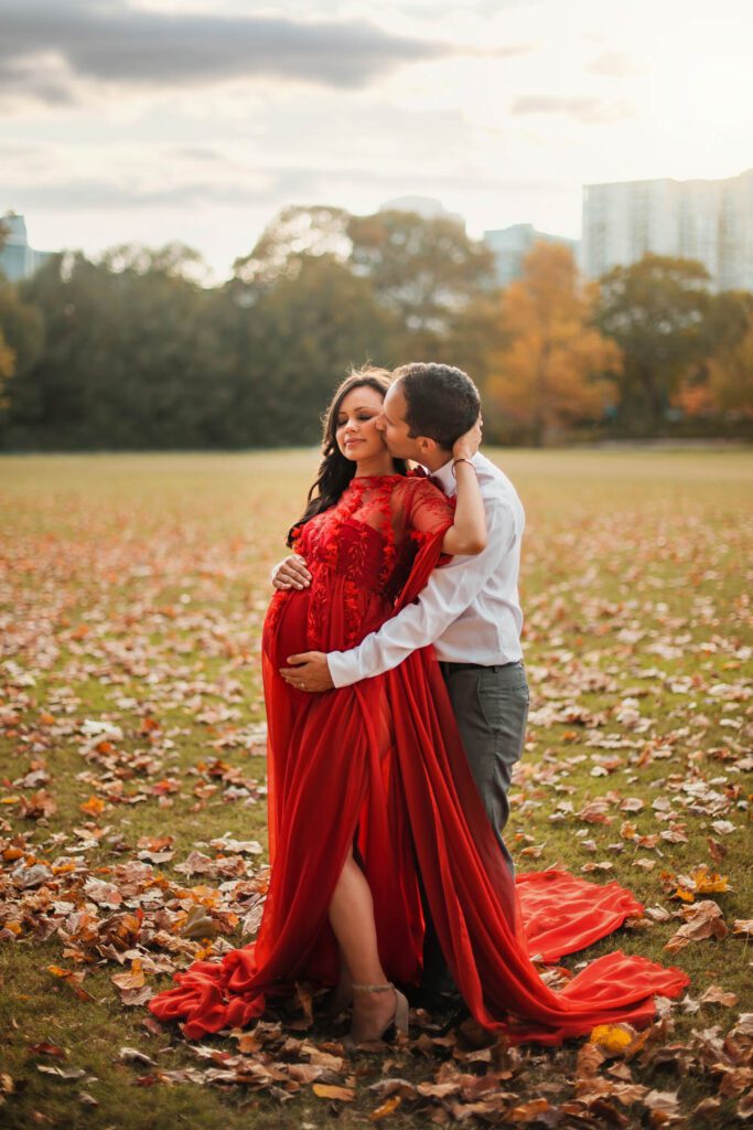 couple embraces among fall leaves with the Piedmont Park Meadow in the background in Atlanta, GA.