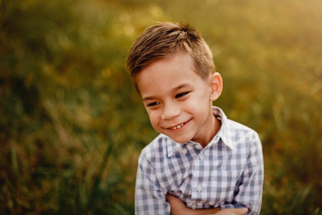Close-up portrait of a smiling son in a checkered shirt with warm golden grass softly blurred behind him.