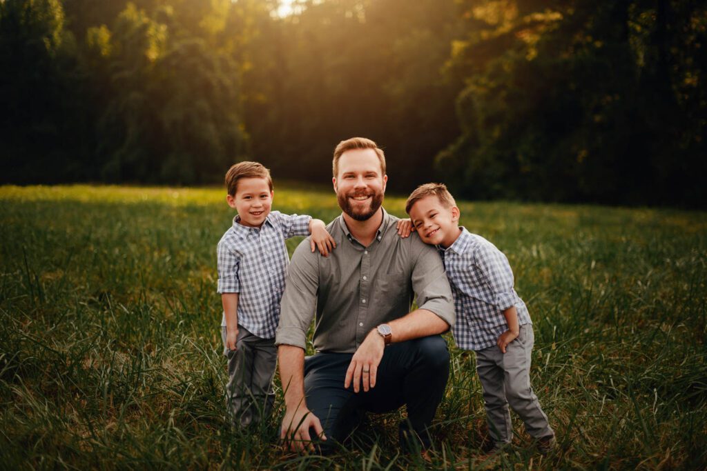 Dad kneeling with his two sons with Garrard Landing Park’s tall grass meadow in the background in Alpharetta, GA.