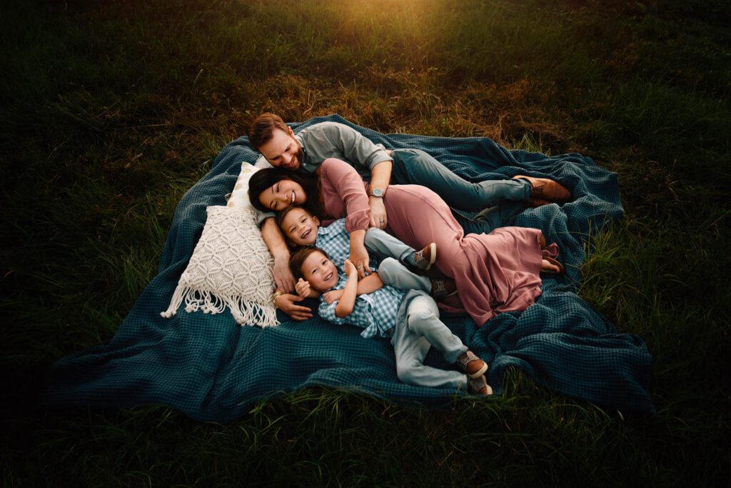 Parents and two sons cuddling on a teal blanket in the tall grass at Garrard Landing Park in Alpharetta, GA.