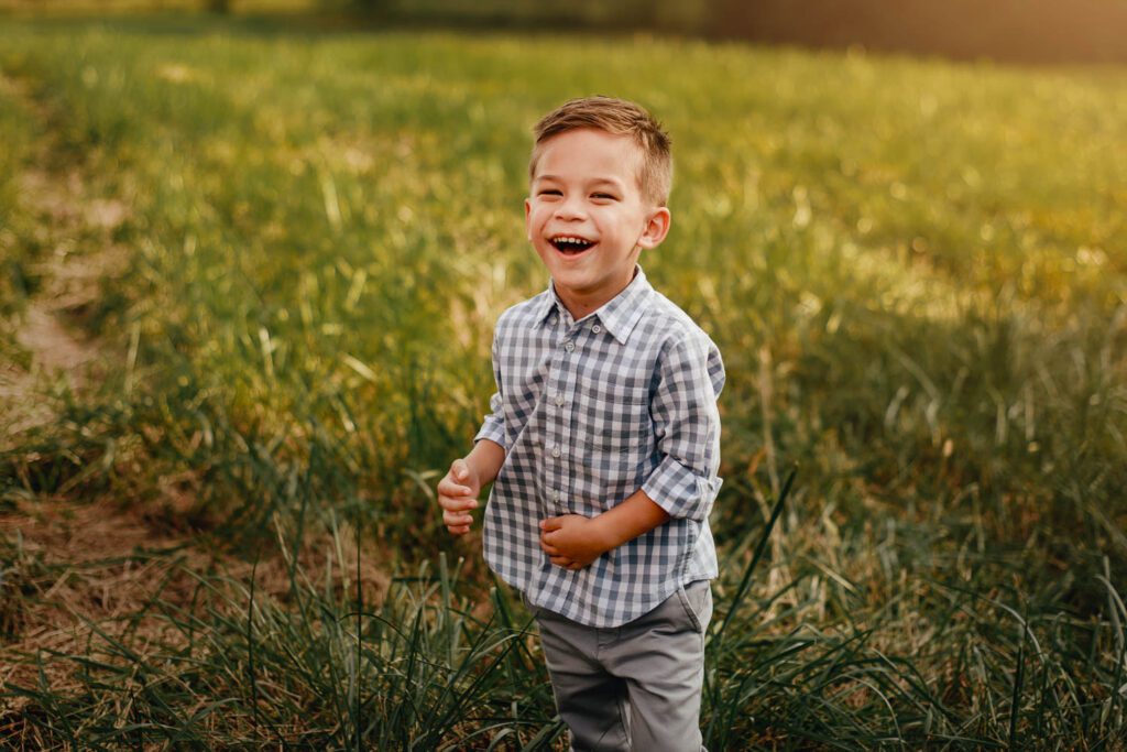 laughing boy in plaid shirt and grey pants in a field of grass