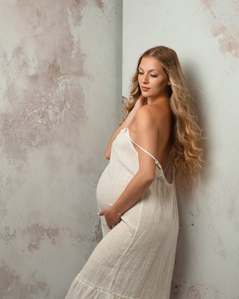 pregnant woman looking down in white dress with one hand gently resting around her belly.