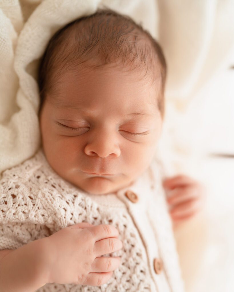 Newborn baby in white knit romper dreaming peacefully on blanket during a studio photoshoot with an Alpharetta newborn photographer. 