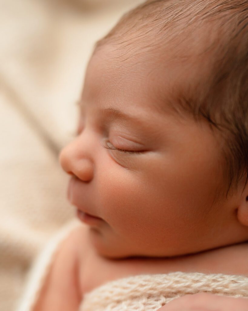 Close-up of a sleeping newborn baby highlighting his profile, eyelashes, and fine dark hair.