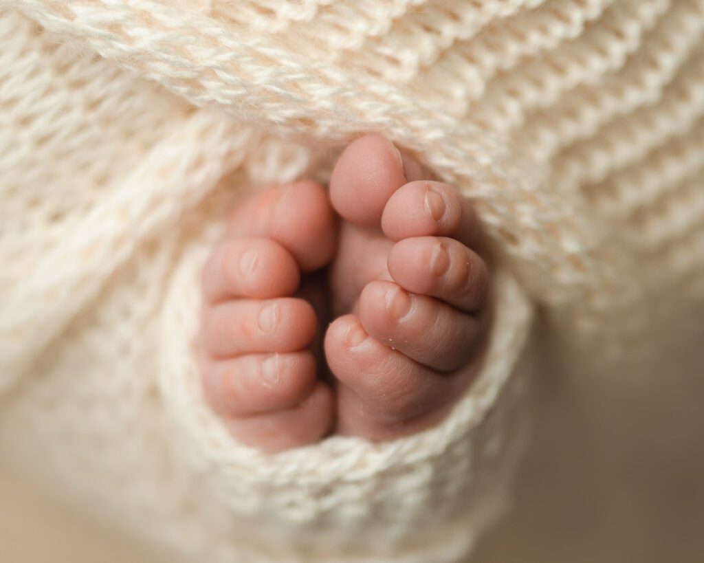 Close-up of a newborn baby’s tiny toes tucked together inside a soft cream knit wrap.