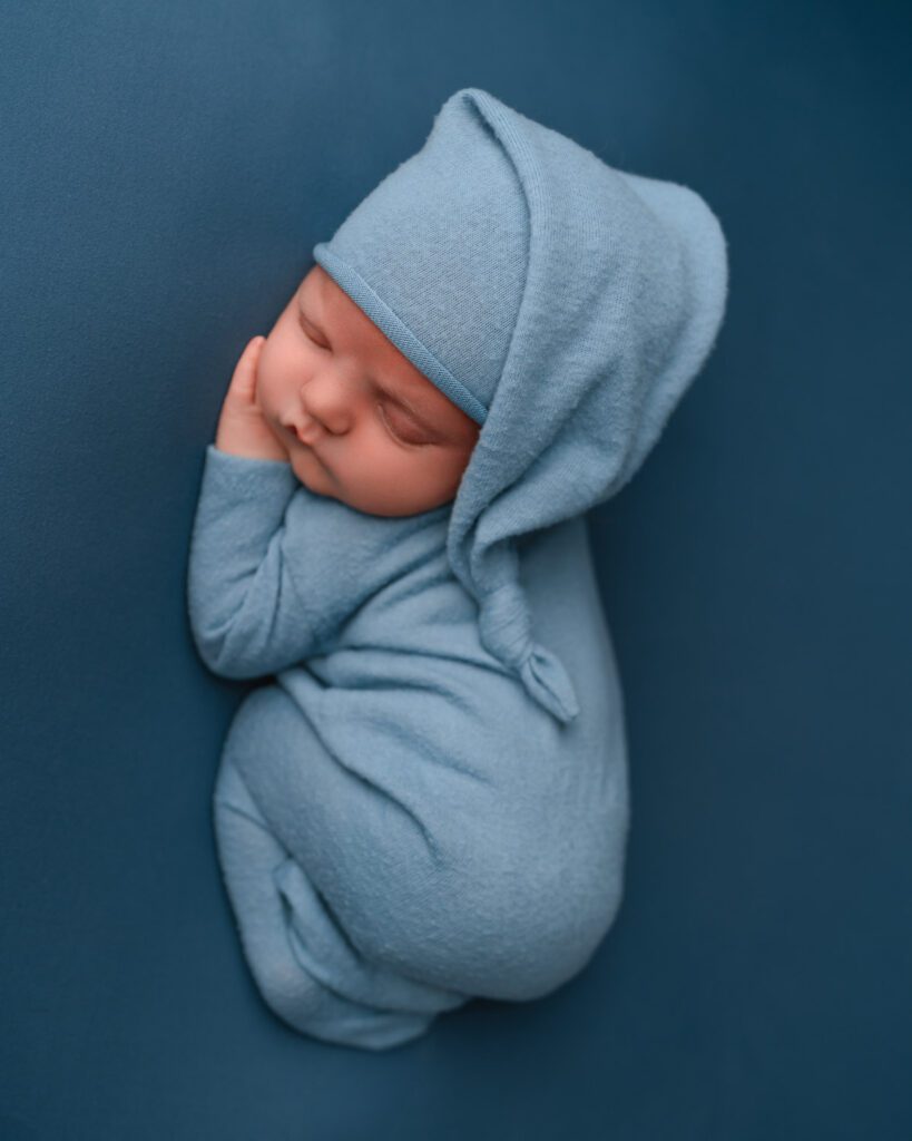 Overhead view of a sleeping newborn baby boy in a soft blue romper and sleepy cap for Atlanta newborn photos.