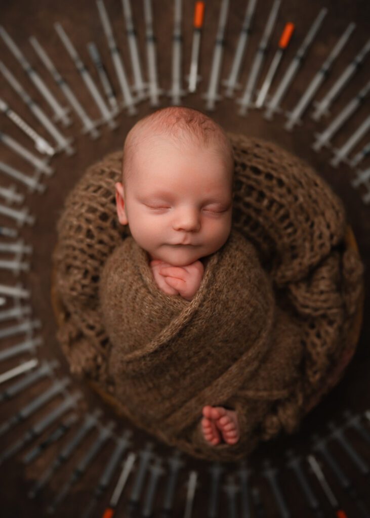 IVF newborn portrait of a baby boy wrapped in brown inside a wooden bowl surrounded by circle of IVF syringes.