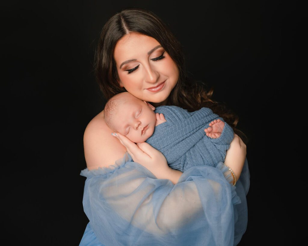 Mom in a sky blue tulle dress lying beside her swaddled newborn baby boy during an Atlanta newborn session.