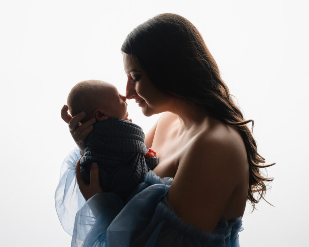 Mom in a blue dress holding her swaddled baby boy against a bright white backdrop during Atlanta newborn photos.