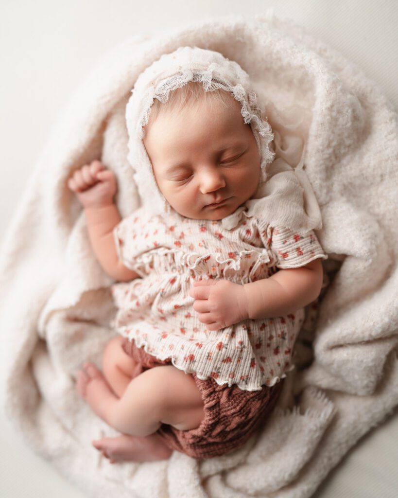 Sleeping newborn baby girl in a ruffled outfit and lace bonnet photographed by an Atlanta newborn photographer.
