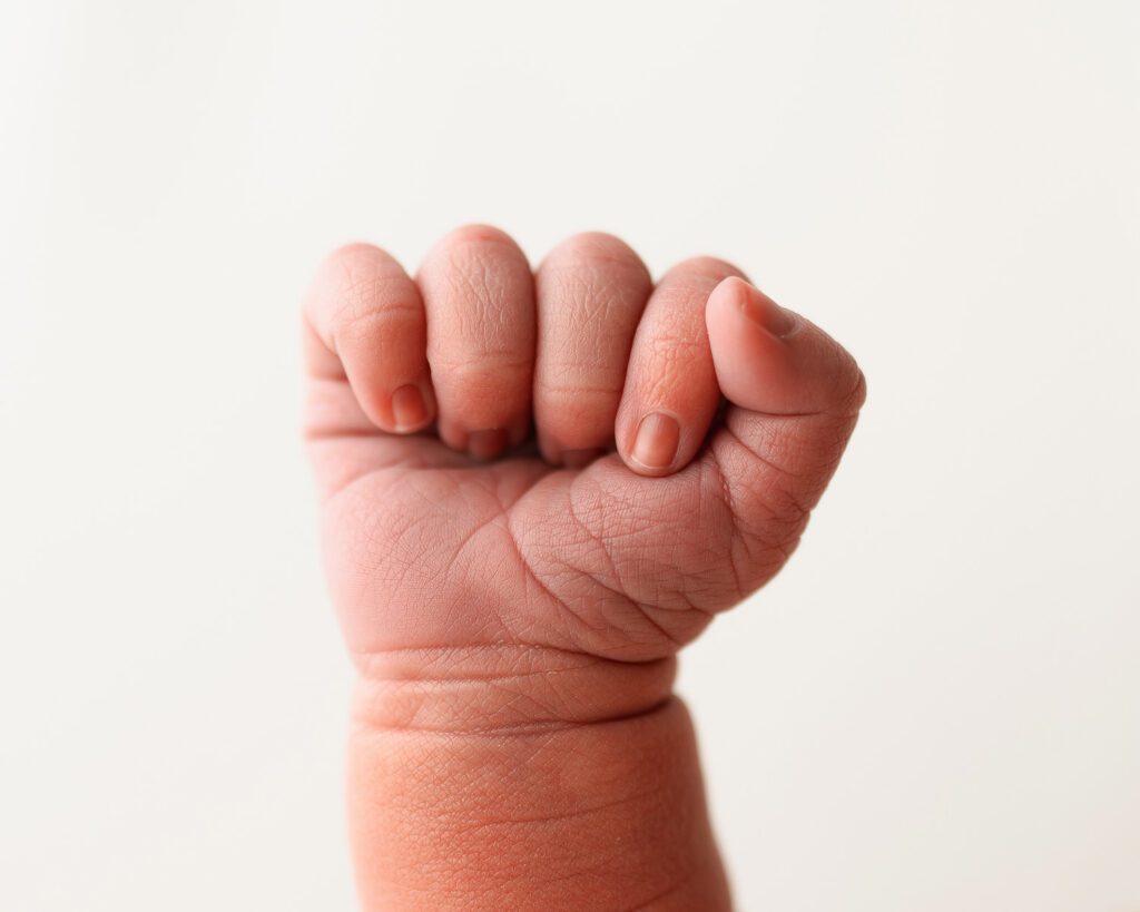 Close-up of a newborn baby’s tiny hand showing delicate wrinkles and fingernails against a white backdrop.