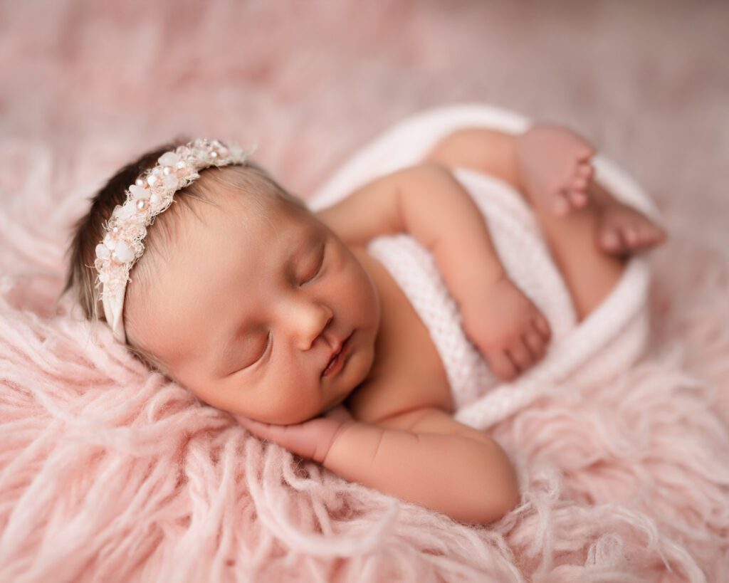 Baby girl wrapped in pink with a pearl headband resting on a soft pink fur blanket during an Atlanta newborn session.