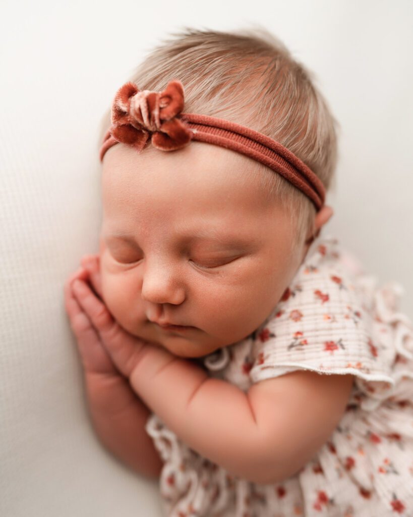 Sleeping baby girl with her hands tucked beneath her cheek during a softly styled newborn portrait session in Atlanta.