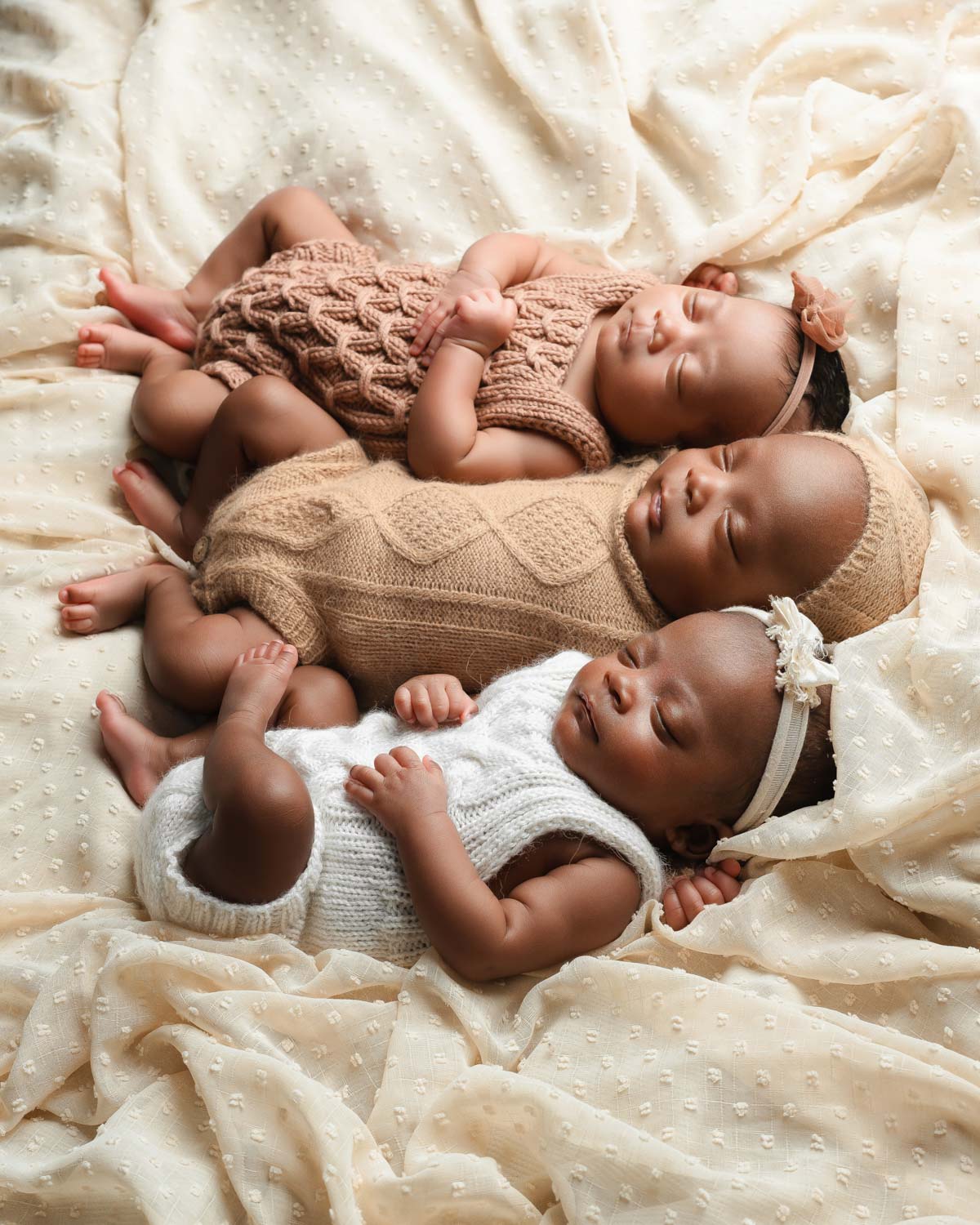 newborn triplets photos with textured outfits laying on neutral fabric sleeping soundly