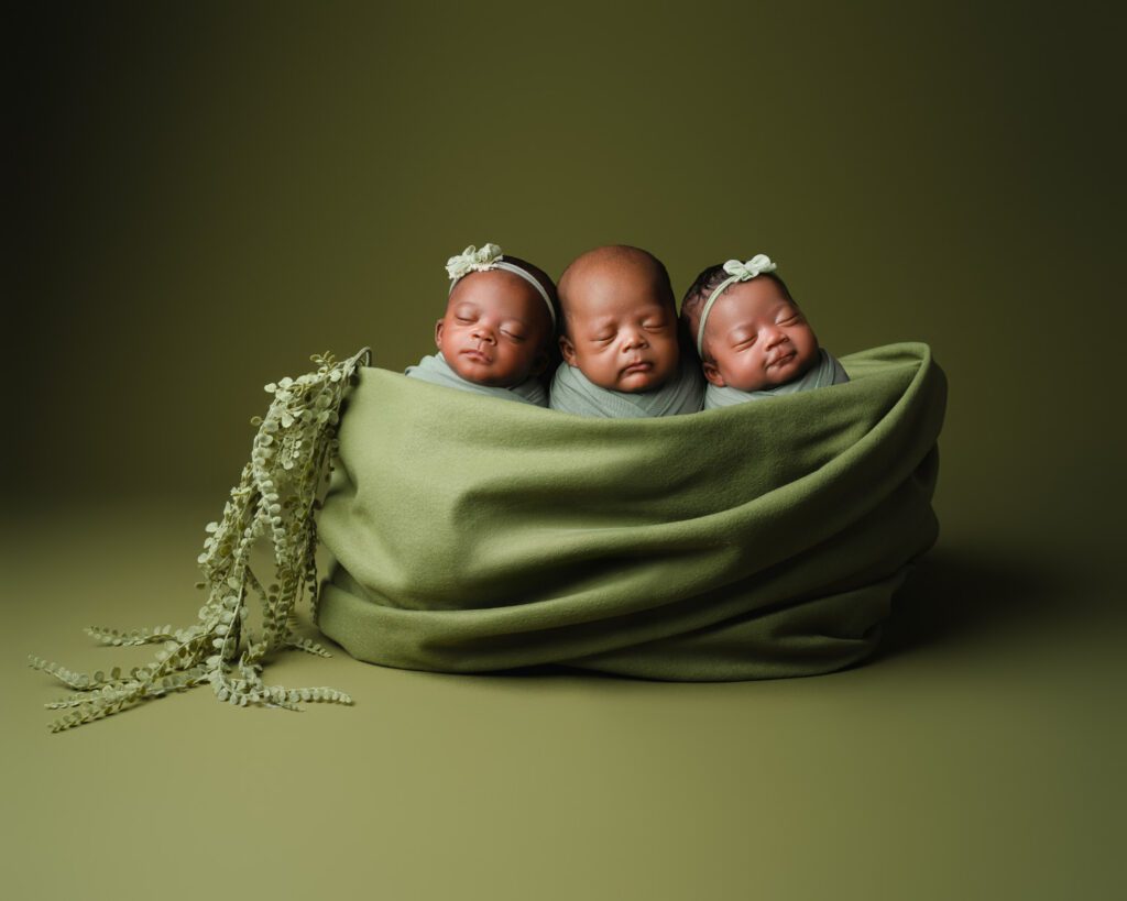 Three newborn triplets swaddled together in pea pod prop against a matching olive studio backdrop.