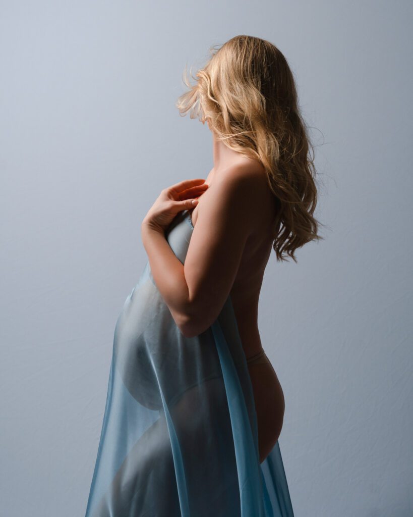 Side-view maternity portrait with flowing blue fabric against a gray backdrop during session with Buckhead maternity photographer.