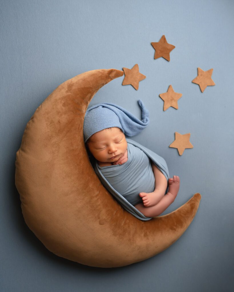 Newborn baby boy in a blue sleepy cap resting on a golden moon pillow with stars