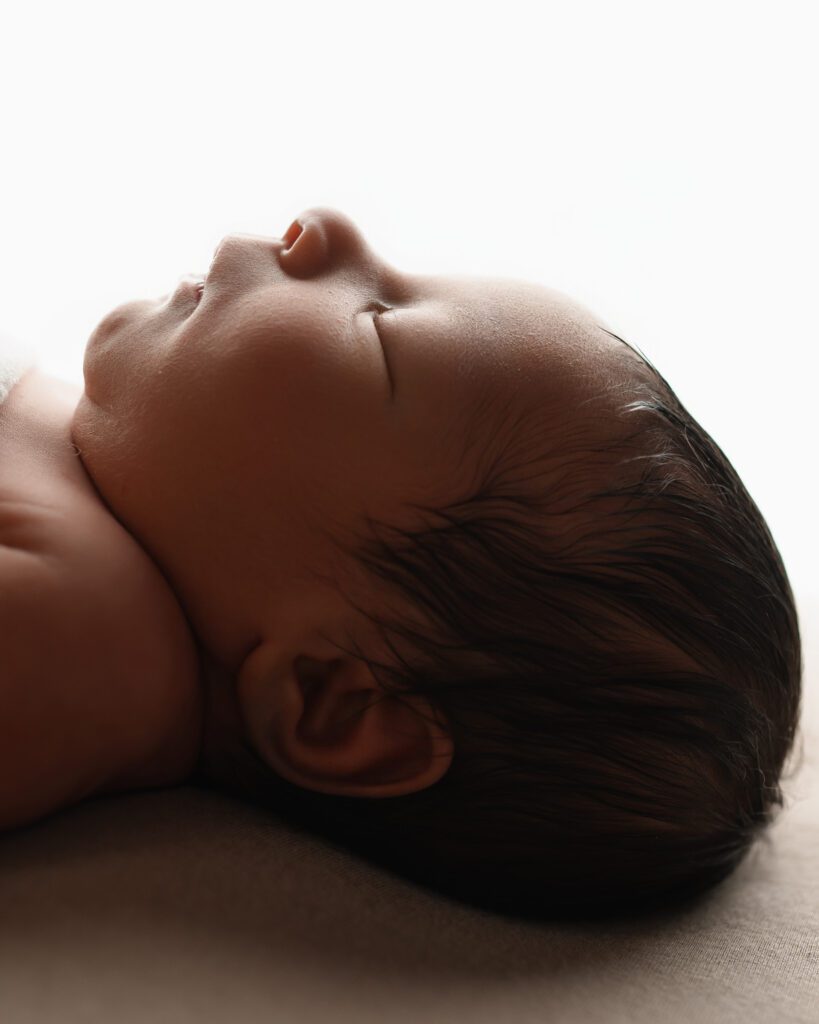 Close-up profile of a sleeping newborn baby resting peacefully against a soft neutral backdrop.