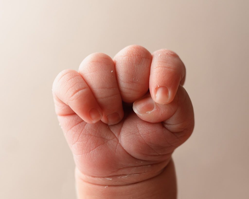 Close-up of a newborn baby hand curled into a fist, showing tiny fingers, wrinkles, and newborn skin.