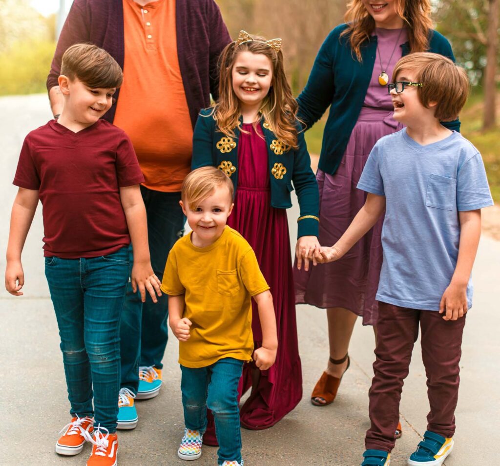 Four siblings walking together with their parents behind them along a tree-lined path.