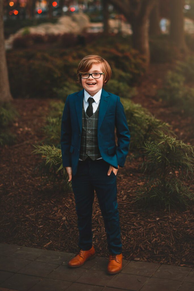 young boy in blue suit and plaid vest standing on paved pathway