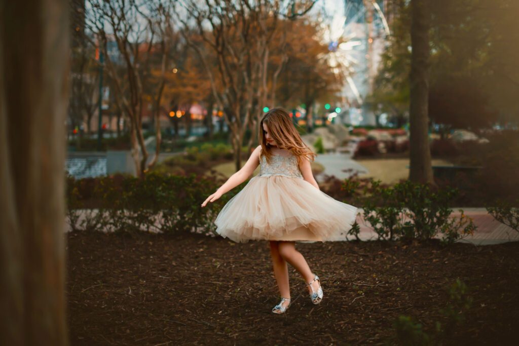 young girl twirls at sunset in sparkly dress outdoors with the Skyview ferris wheel in the background.