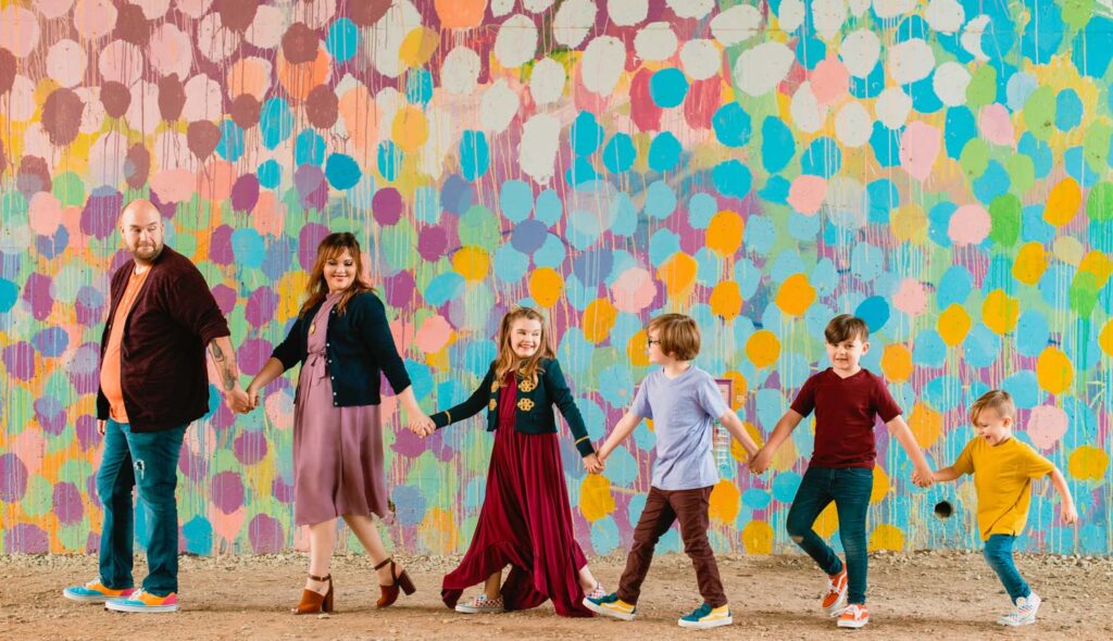 Parents and four children holding hands in a line beside the Confetti Mural on the Atlanta BeltLine Eastside Trail.