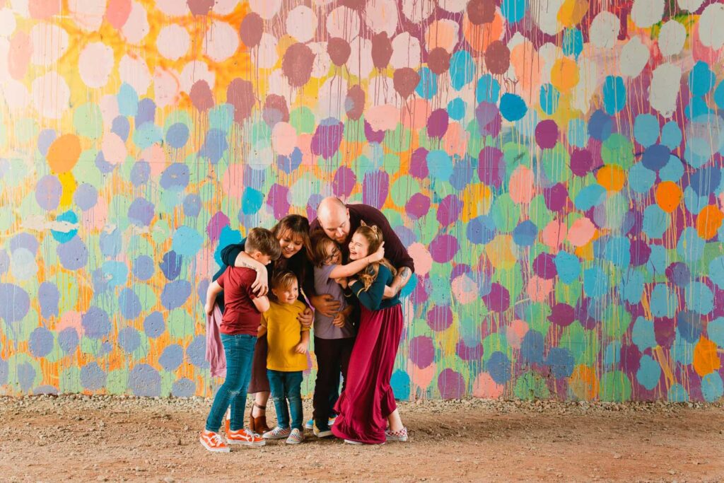 Parents and four children cuddling together with the Atlanta BeltLine Confetti Mural in the background in Atlanta, GA.