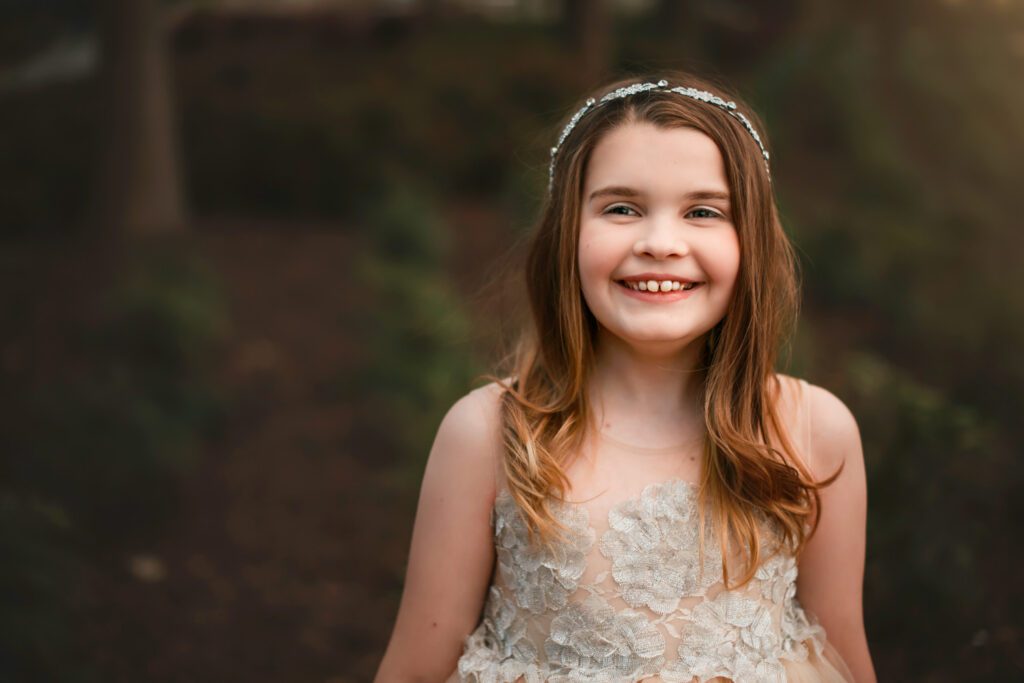 close up of smiling tween girl in sparkly ivory dress with headband in her hair looking at camera.