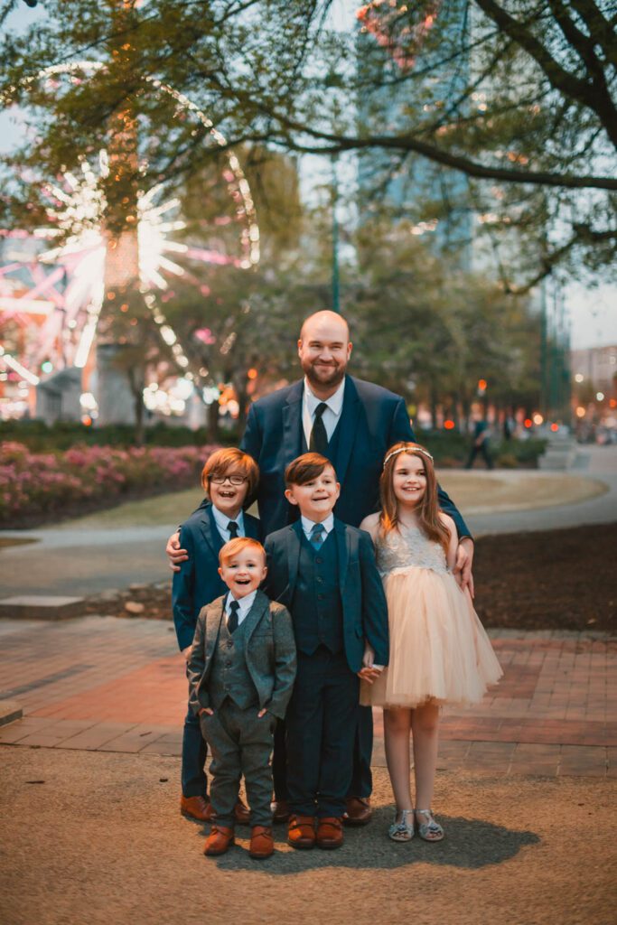 father and four children standing together with the Centennial Olympic Park SkyView Ferris Wheel in the background in Atlanta, GA
