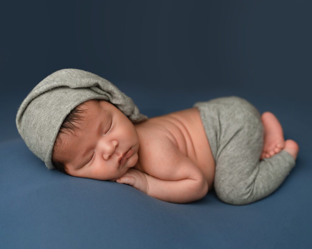 five week old newborn baby boy wearing grey pants and a matching sleepy cap hat during a newborn session. 