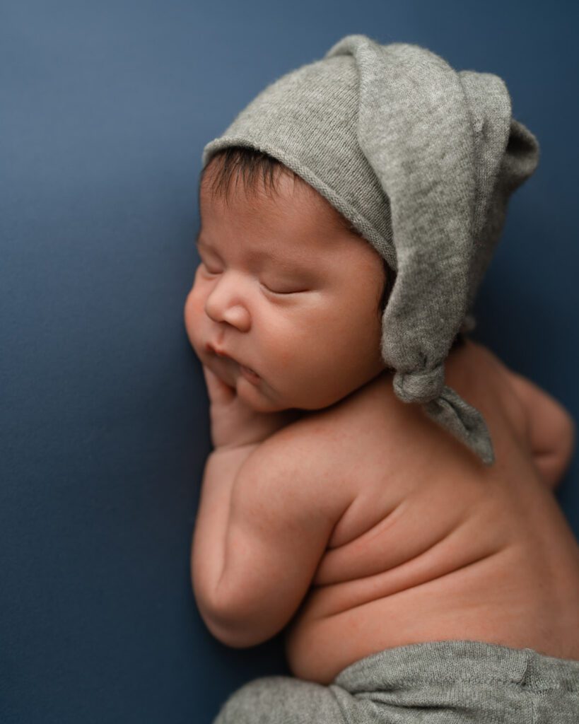 five week old newborn baby boy wearing grey sleeping hat laying on his tummy on a blue fabric background. 