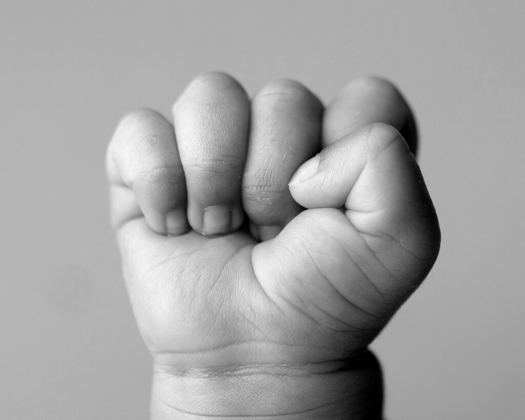 closeup of newborn baby hand curled up in a ball showcasing the tiny details like skin flakes and finger wrinkles in black and white