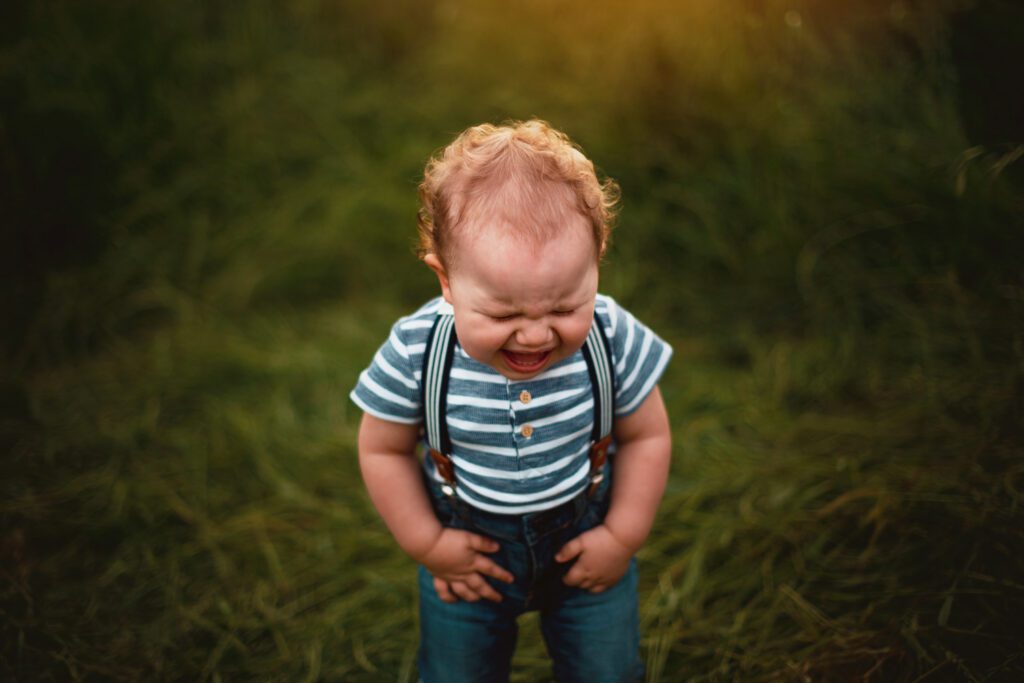 toddler boy in stripe shirt and suspenders and jeans having tantrum in open meadow at sunset