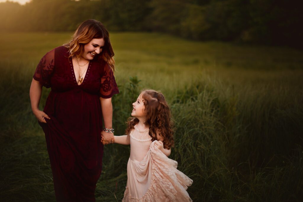 mom and daughter walking hand in hand looking up at each other smiling in a meadow at Kennesaw Mountain in Marietta, GA