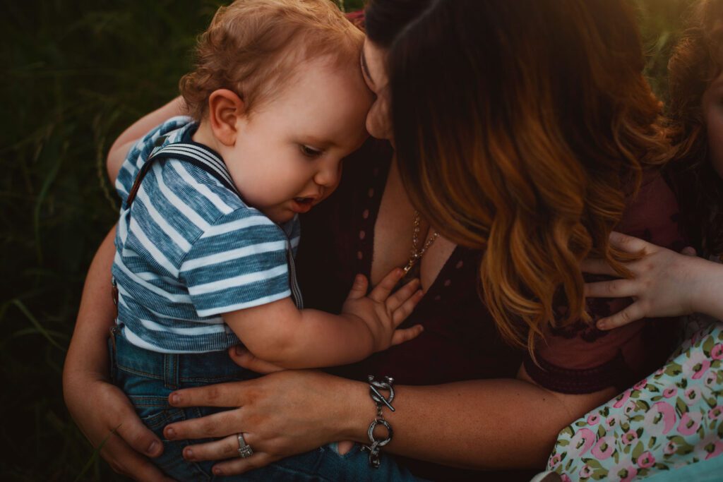 Close-up of mom pressing her forehead to her baby son while holding him gently in warm evening light.