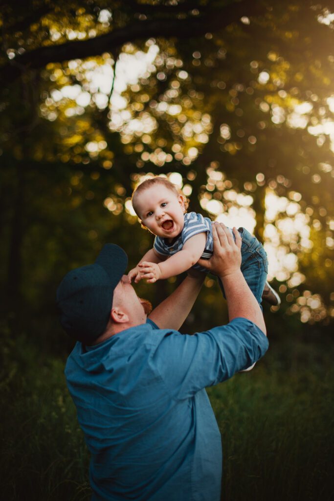 dad lifting up toddler son in the air at golden hour near the trees
