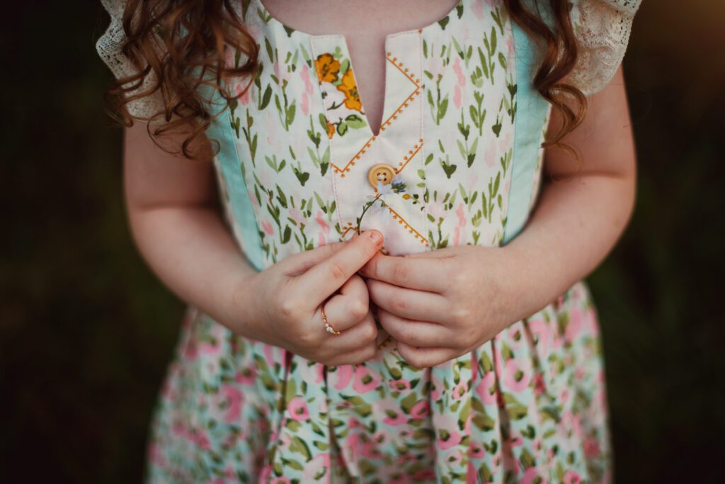 Close-up of a young girl in a floral dress holding her hands together against a softly blurred meadow.