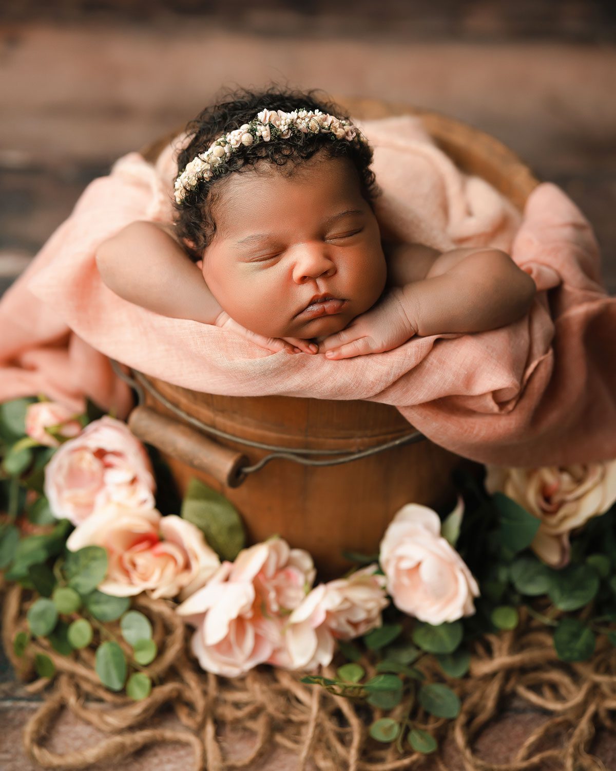 Sleeping newborn in wood bucket wearing floral headband with roses at photographed by marietta newborn photographer.