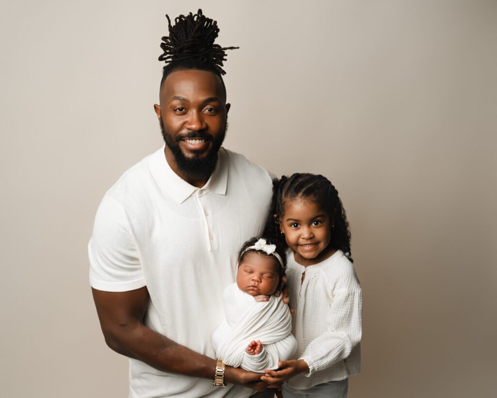 Dad holding his newborn daughter with big sister beside him for a Marietta newborn photographer session.