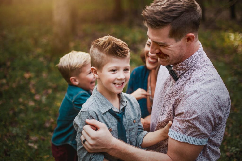 Dad laughing with his two sons while holding them close in warm outdoor light.