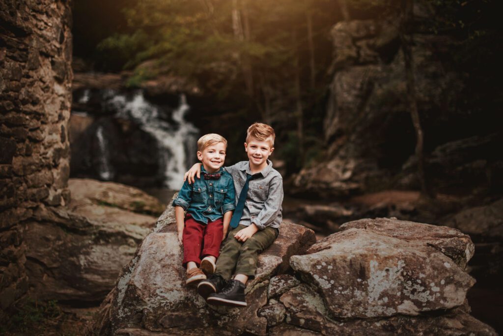 Two brothers sitting on old mill ruins with a cascading waterfall behind them.