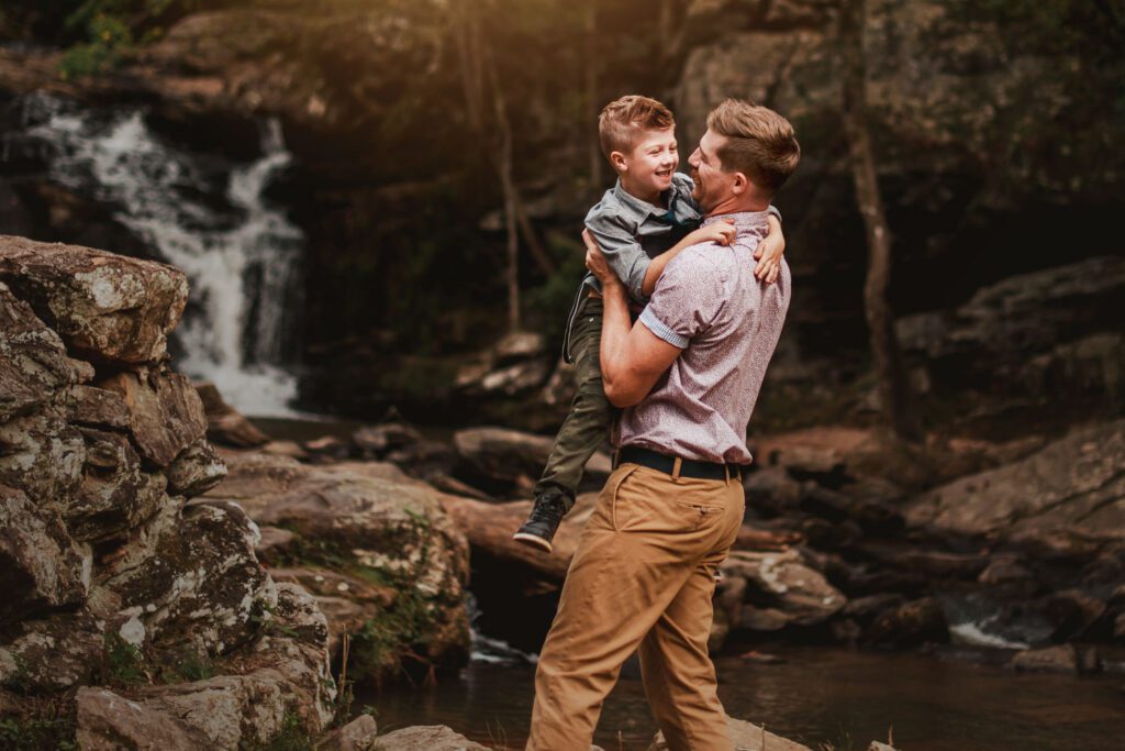 Dad holding his young son beside a rocky creek with Cochran Mill Falls in the background in Chattahoochee Hills.